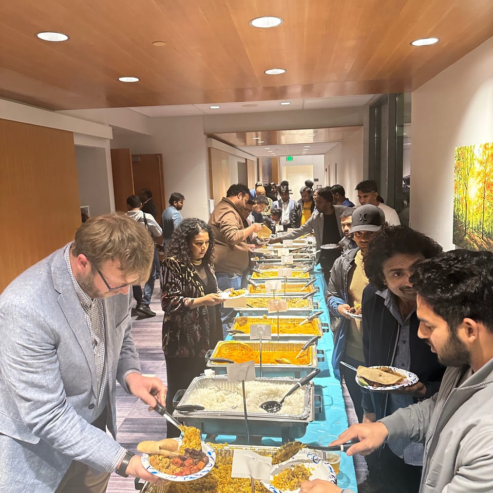 Crowded restaurant buffet with diners serving rice, curries, and other dishes from chafing trays.