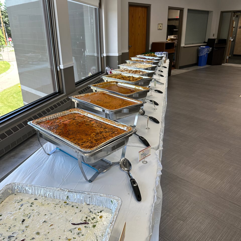 Buffet table lined with chafing dishes of assorted hot foods and creamy salad in a bright dining room.