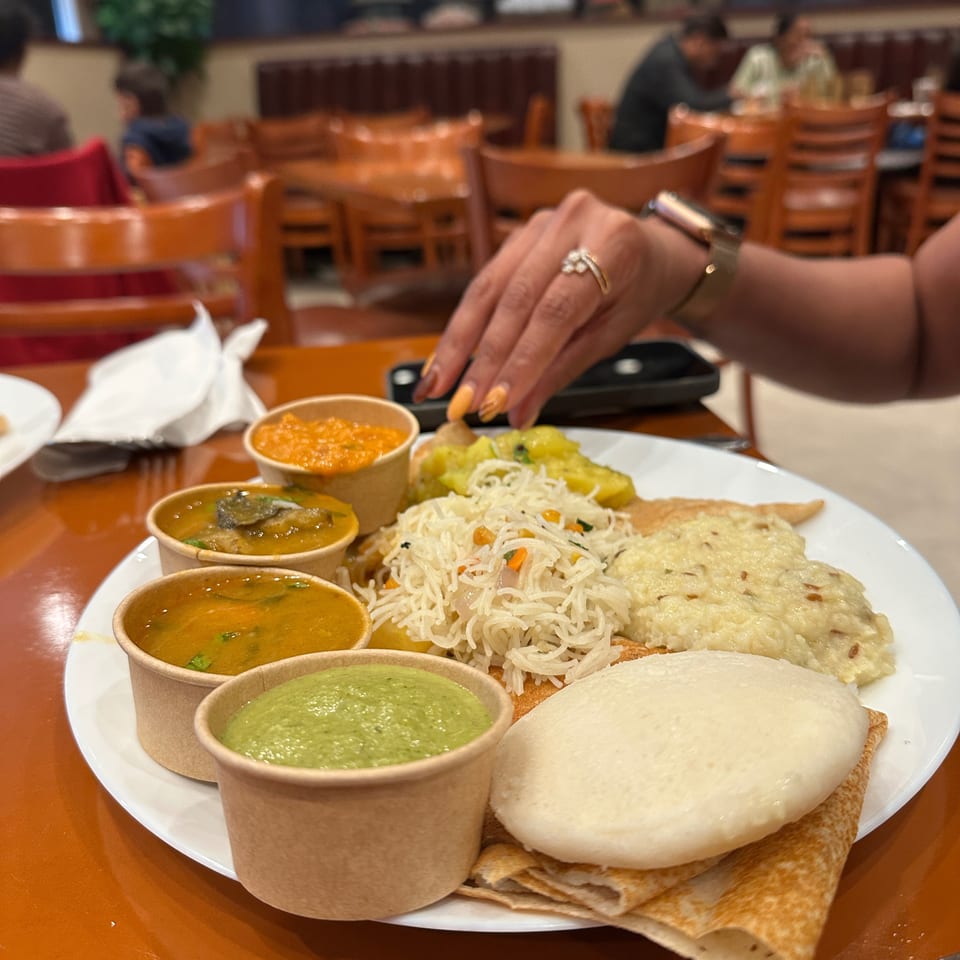 Indian thali platter with naan, rice noodles, curries, chutneys, and papadum on a restaurant table.
