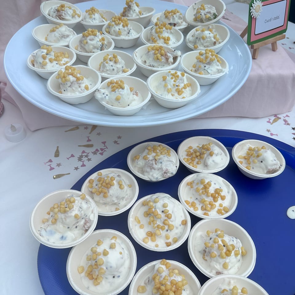 Small bowls of creamy curd vadas topped with boondi arranged on white and blue serving trays at an outdoor food stall.