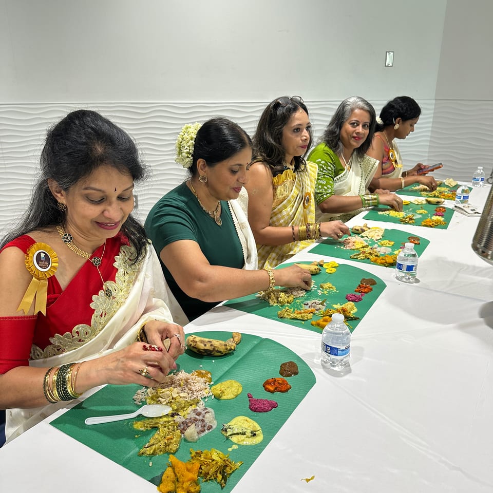 Women in traditional Indian attire eat a colorful vegetarian meal served on banana leaves at a banquet table.
