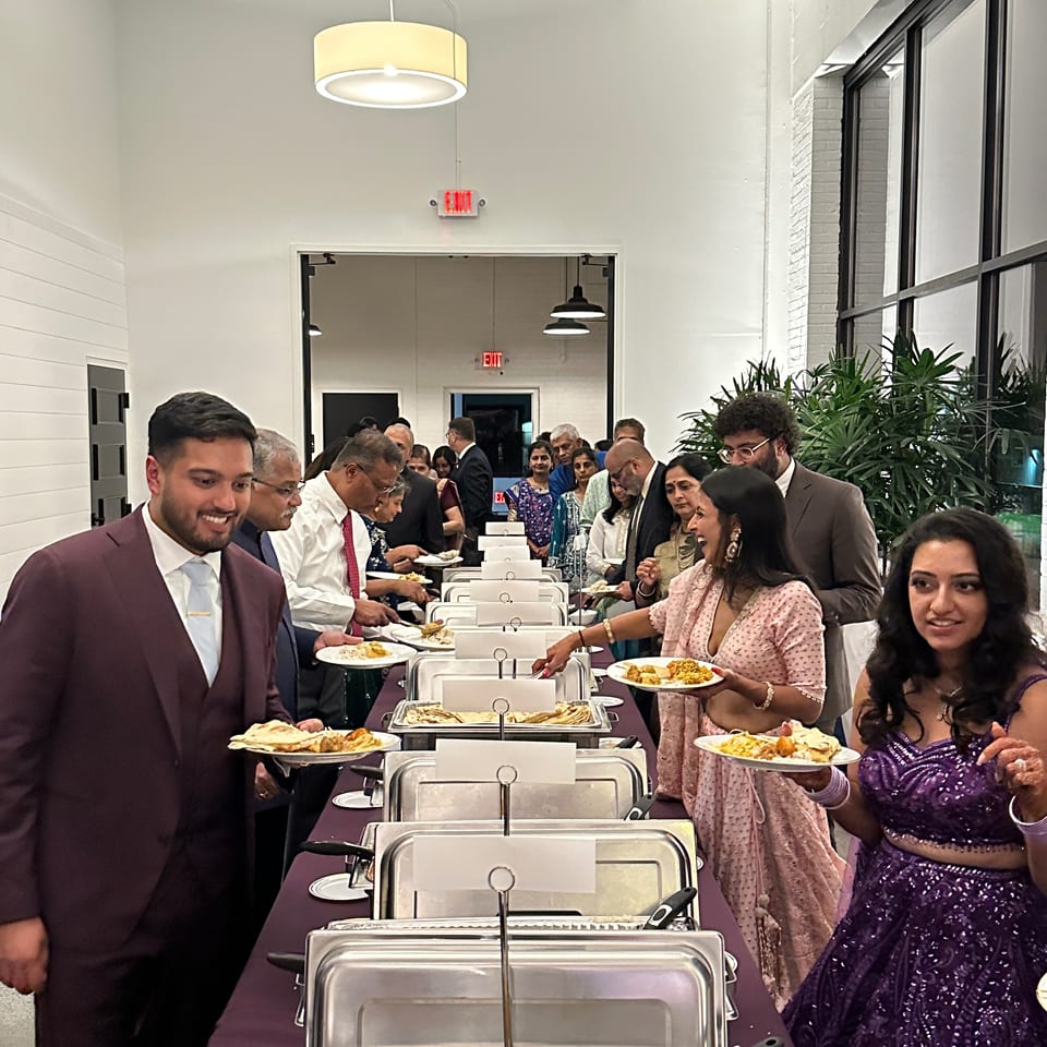 Guests serve themselves Indian dishes from stainless-steel chafing dishes at a busy restaurant buffet.